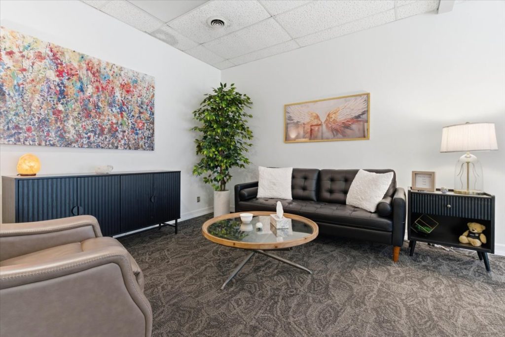 Therapy office lounge with a black leather sofa and colourful abstract artwork