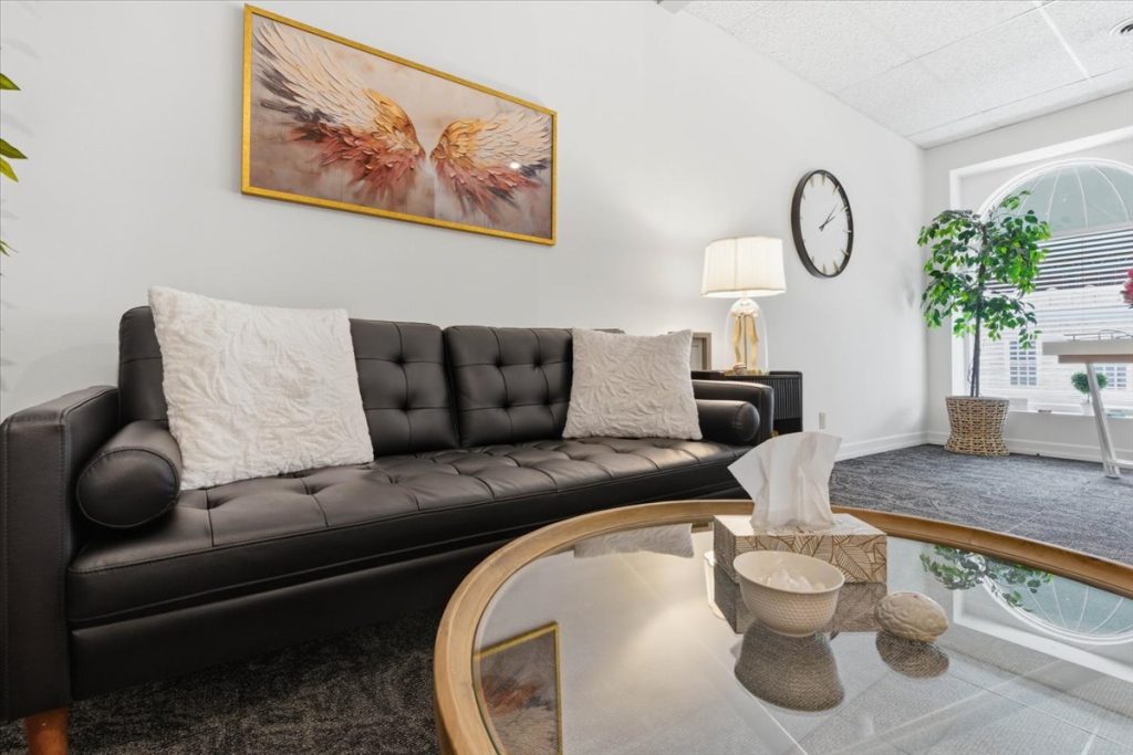 Therapy office lounge with a black leather sofa, glass coffee table and wing artwork